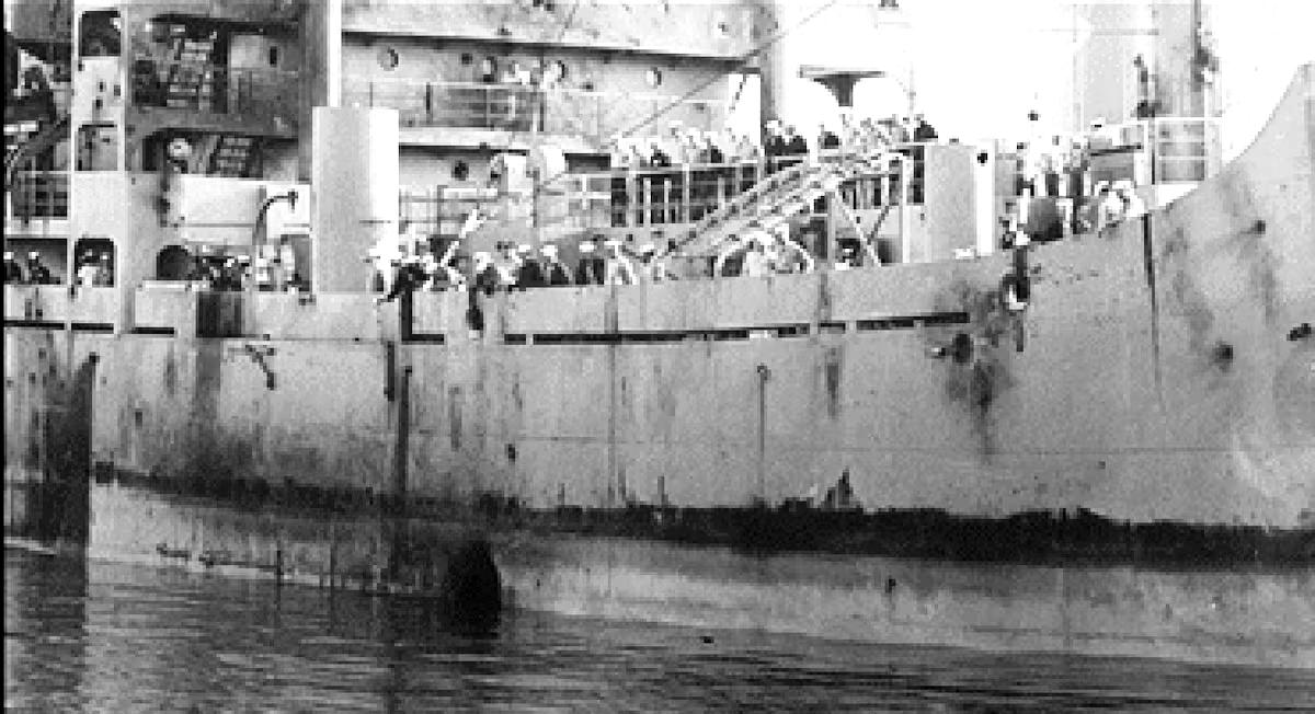 U.S.S. Liberty crew gather on deck to examine huge torpedo hole at the ships waterline. (U.S. Navy)