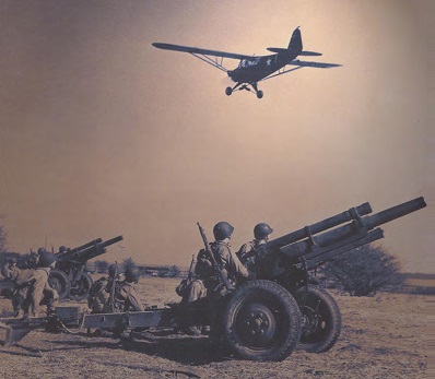 J-3 Cub, in Army olive-drab green, as L-4, flys over U.S. artillery it guides in World War II
